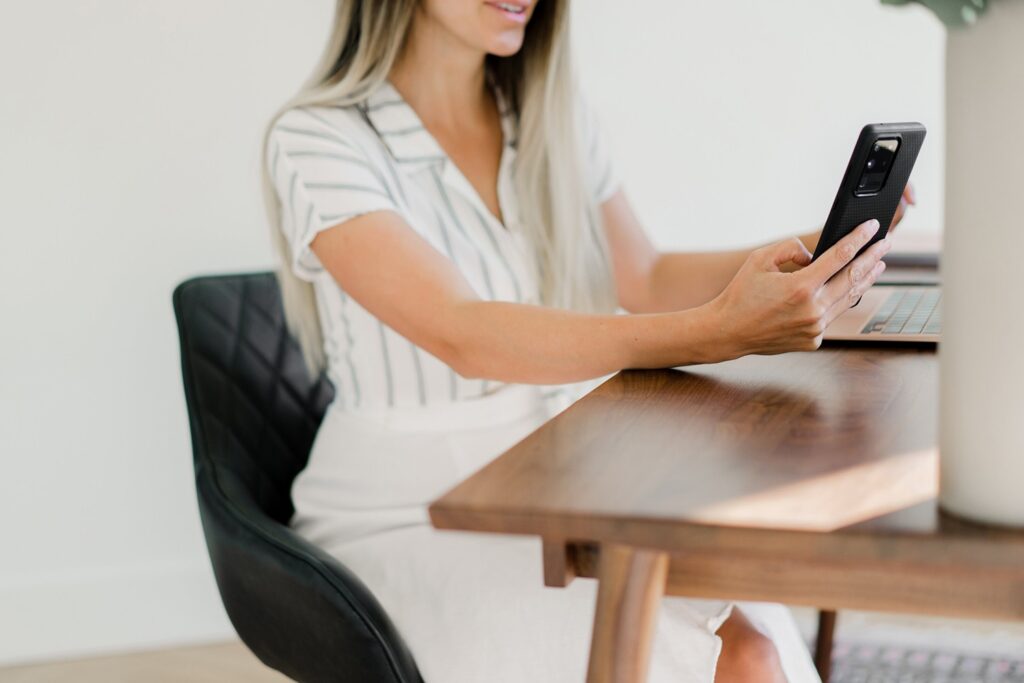 Bridal makeup artist working at her computer and holding a phone.